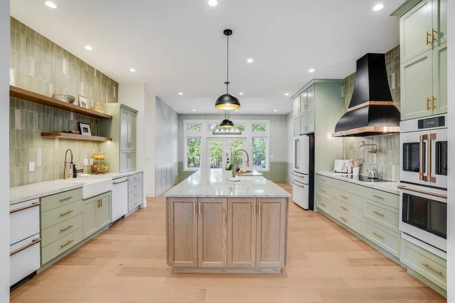 Spacious kitchen with sage cabinets, wood island, and copper range hood.