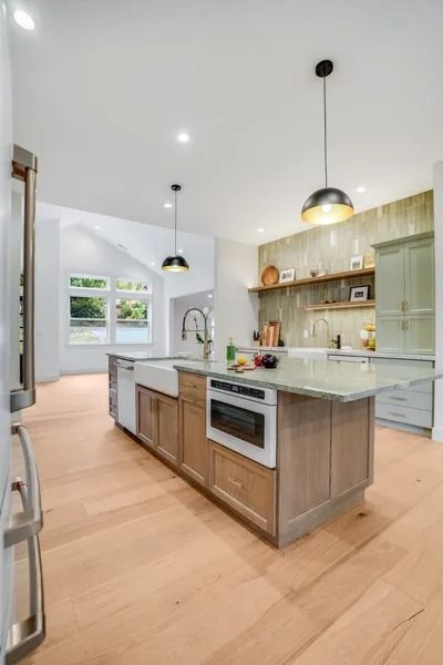 Modern kitchen with light wood floors and island, stainless steel appliances, and two pendant lights.