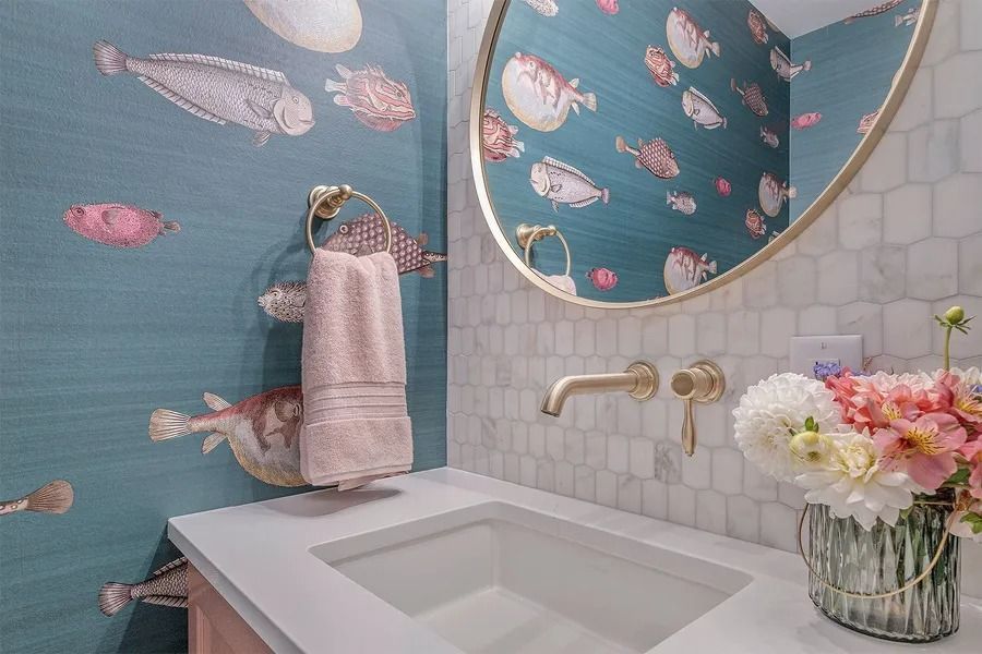 Powder room with fish wallpaper, gold fixtures, marble backsplash, and a pink towel.