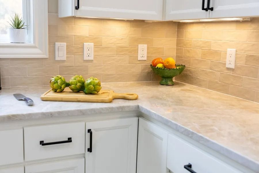 Kitchen counter with artichokes, fruit bowl, and white cabinets.