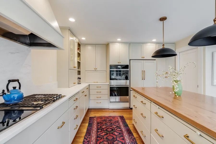 Modern kitchen with light cabinets, wood countertops, and a patterned rug.
