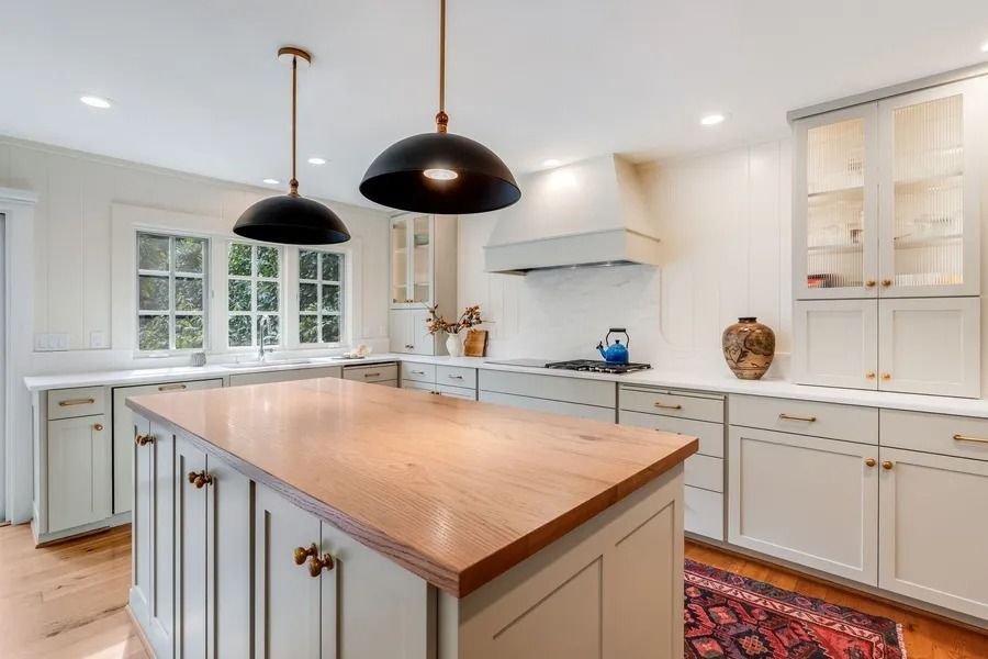 Kitchen with light grey cabinets, wooden island, black pendant lights, and window.