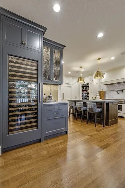 Modern kitchen with blue cabinetry, wine fridge, wood floors, and island with bar stools.