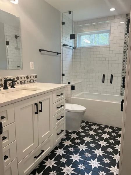 Bathroom with white vanity, black hardware, subway tile shower, and patterned black and white floor tiles.