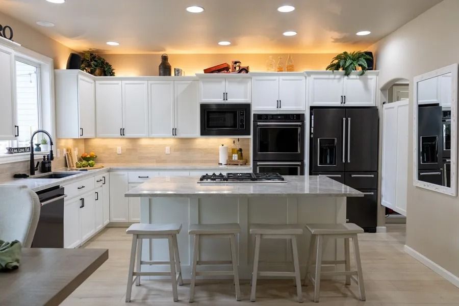 White kitchen with island, black appliances, and overhead cabinets with recessed lighting.