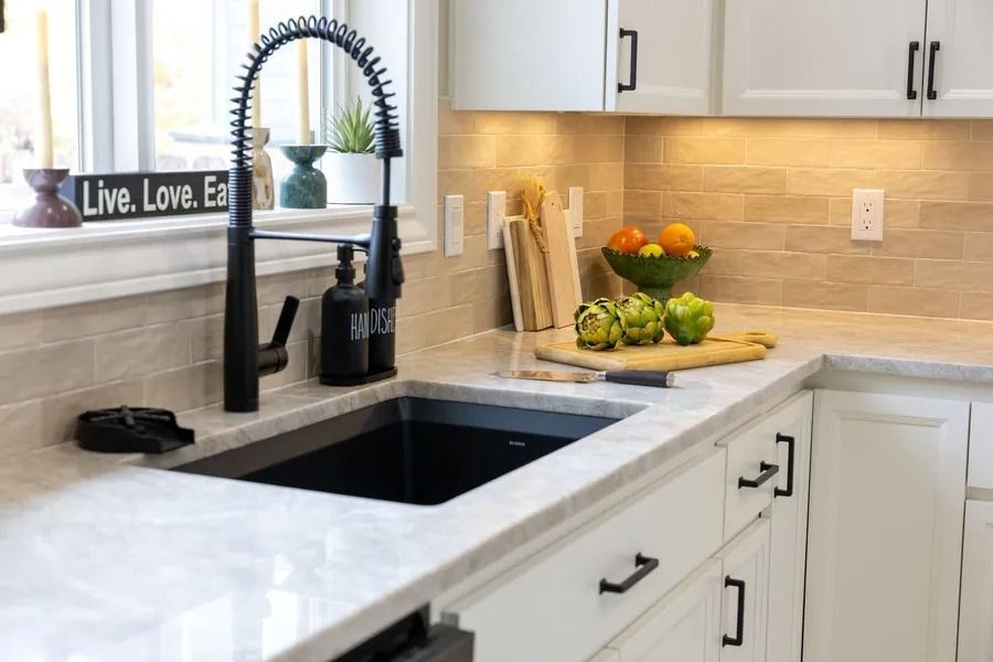 Black kitchen sink with a gooseneck faucet. White cabinets, marble countertops, and artichokes.
