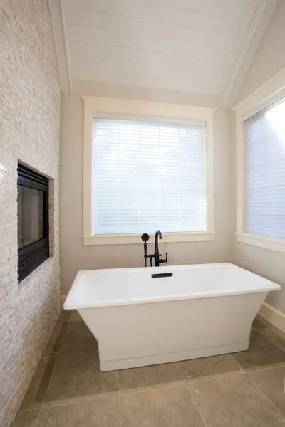 White bathtub in a modern bathroom with a window and fireplace.