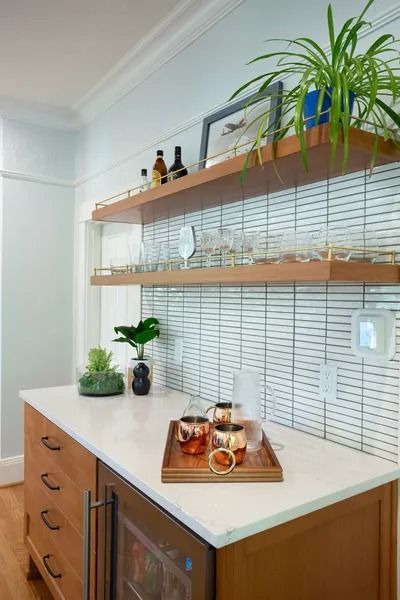 Home bar with wood cabinetry, white countertop, floating shelves, and tiled backsplash.