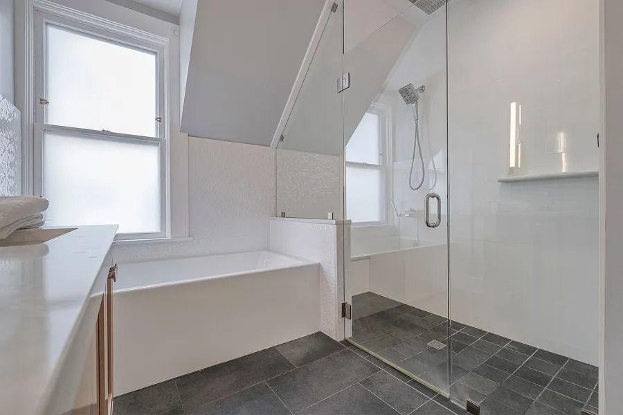 Bathroom with white walls, window, built-in tub, glass shower, and gray tile floor.