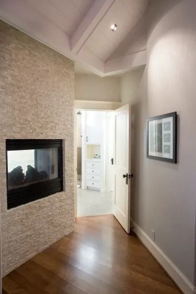 Hallway with fireplace, light walls, wooden floor. Open doorway leads to a bright room.