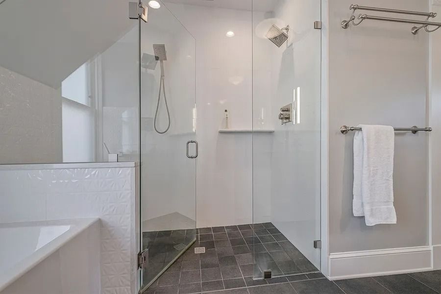 Modern bathroom with glass shower, white walls, gray tiled floor, and a towel rack with a white towel.