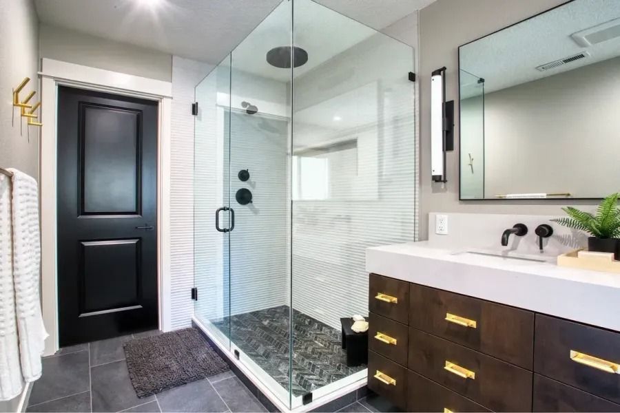 Modern bathroom with glass shower, dark wood vanity, black door, and gray tile.