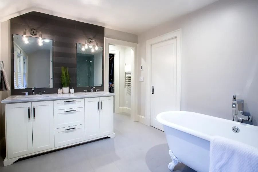 White bathroom with double vanity, tub, and dark wood accent wall.