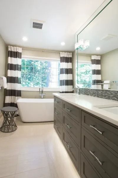 Modern bathroom with a white tub by a window, gray vanity, and striped curtains.
