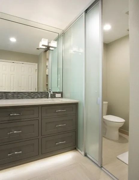 Bathroom with gray vanity, large mirror, frosted glass sliding door leading to toilet.