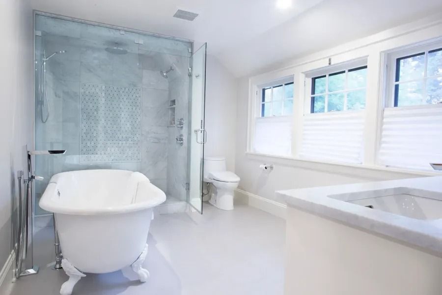 Bright white bathroom with a clawfoot tub, glass shower, toilet, and marble vanity.