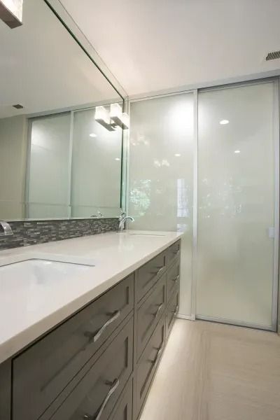 Modern bathroom with gray cabinets, white countertop, and sliding glass door.
