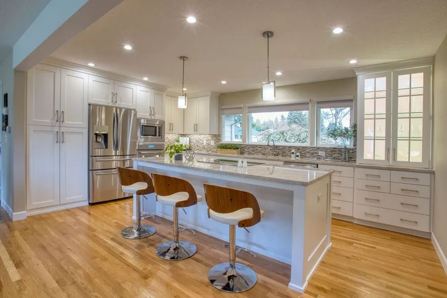 Modern kitchen with white cabinets, island with stools, stainless steel appliances, and wood floor.