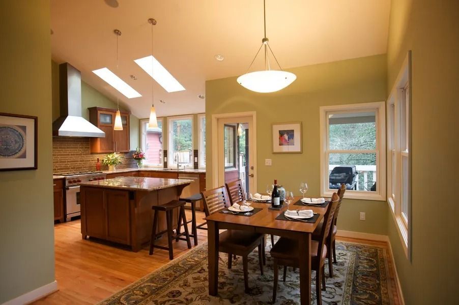 Kitchen with island, dining table, and natural light, featuring green walls and wooden cabinets.