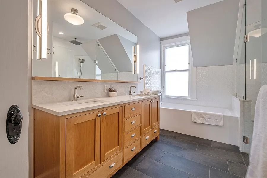 Bathroom with wooden vanity, large mirror, and soaking tub by a window.