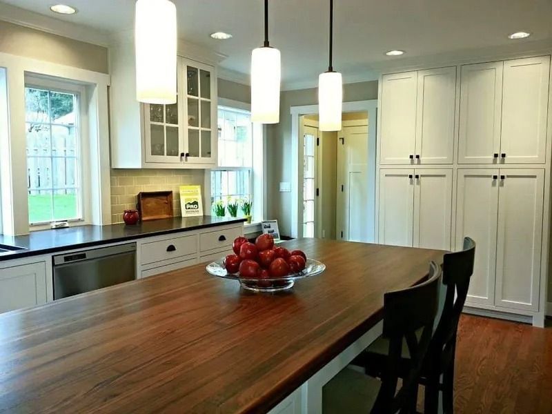 Kitchen with white cabinets, wood island, pendant lights, and red apples.