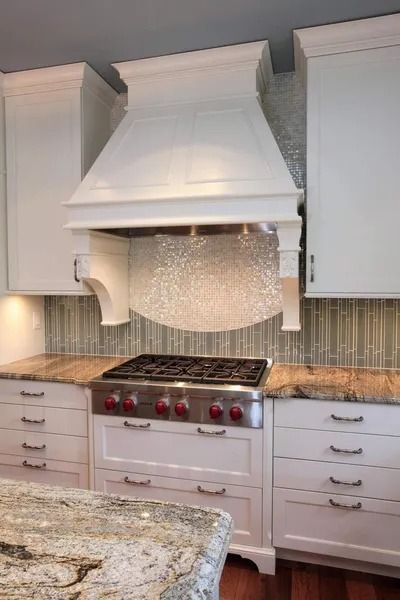 White kitchen with stove, range hood, and cabinets. Backsplash is glass tile. Granite countertop.
