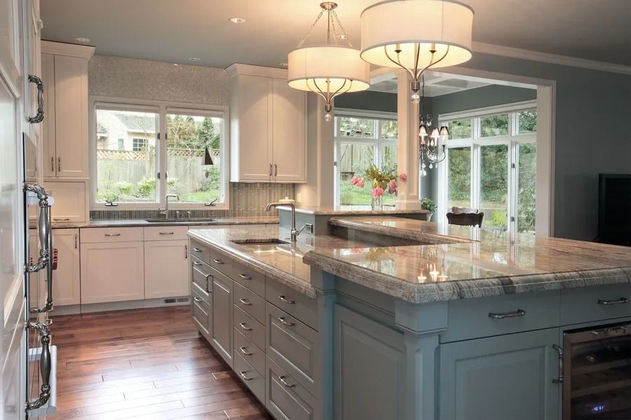 Kitchen with white cabinets, blue island, granite countertop, pendant lights, and window.