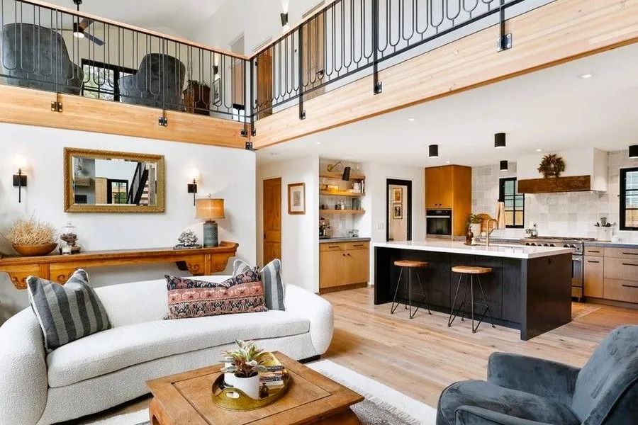 Open-concept living space with loft. White walls, wood accents, black island, kitchen, sofa, and armchair.