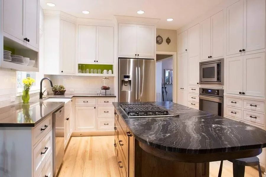 White kitchen with island and black countertops, stainless steel appliances, and wooden floors.