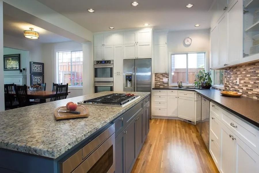 Kitchen with granite island, white cabinets, stainless steel appliances, and wooden floors.