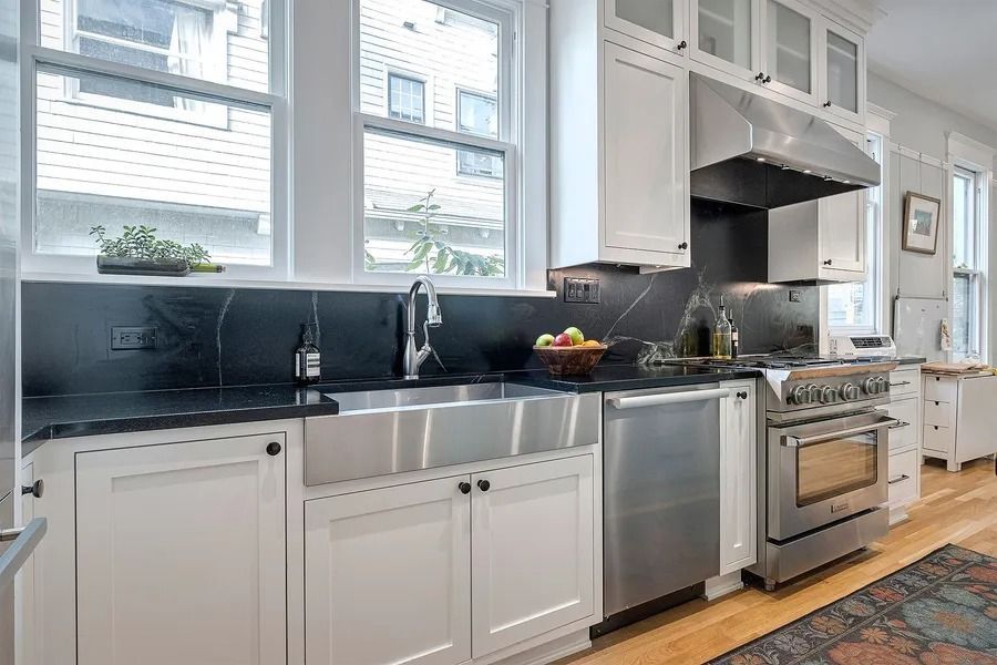 Stainless steel kitchen with white cabinets, black countertops, and a large window.