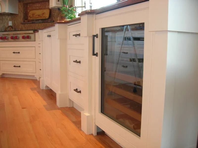 White kitchen cabinets with a built-in glass-door wine cooler, hardwood floor.