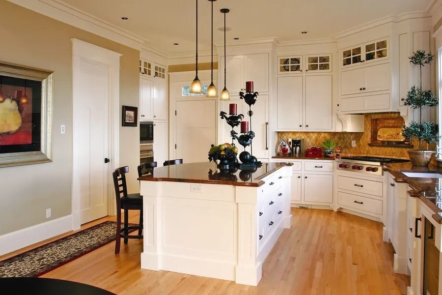 Elegant white kitchen with island, brown countertop, pendant lights, wood floor.