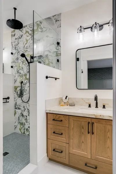 Bathroom with wood vanity, marble countertop, glass shower, patterned tile, and black fixtures.