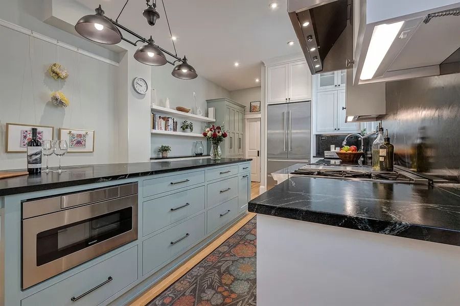 Kitchen with blue cabinets, black countertops, stainless steel appliances, and a patterned rug.