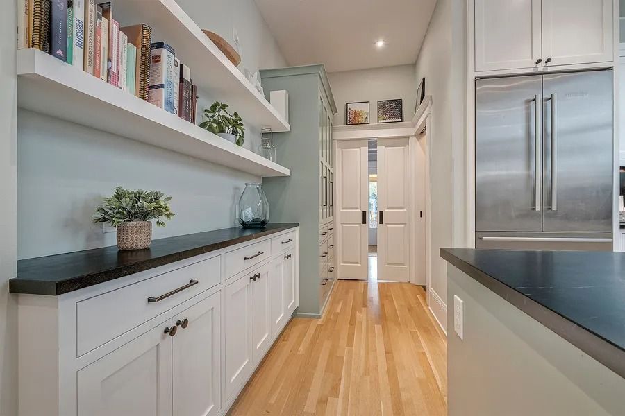Kitchen with white cabinets, shelves, black countertop, stainless steel refrigerator, and wood floor.