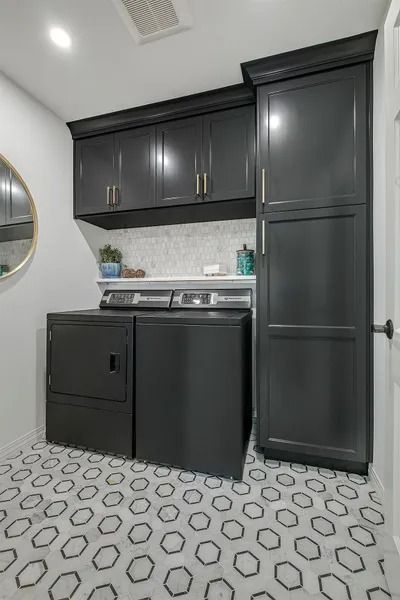 Dark gray laundry room with patterned floor, washer, dryer, cabinets.