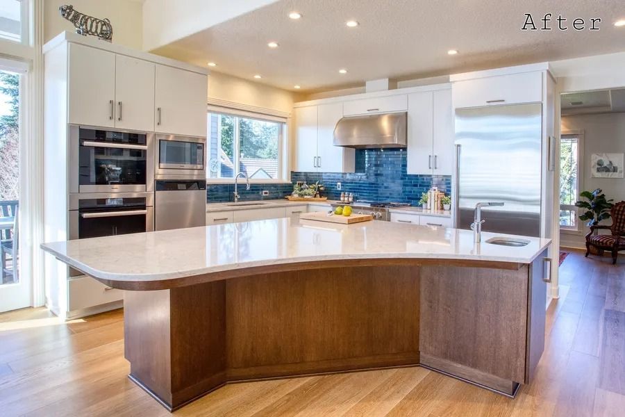 Modern kitchen renovation with white cabinets, wood island, stainless steel appliances, and wood flooring.