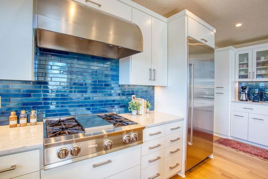 Kitchen with blue tile backsplash, stainless steel appliances, white cabinets, and light countertop.