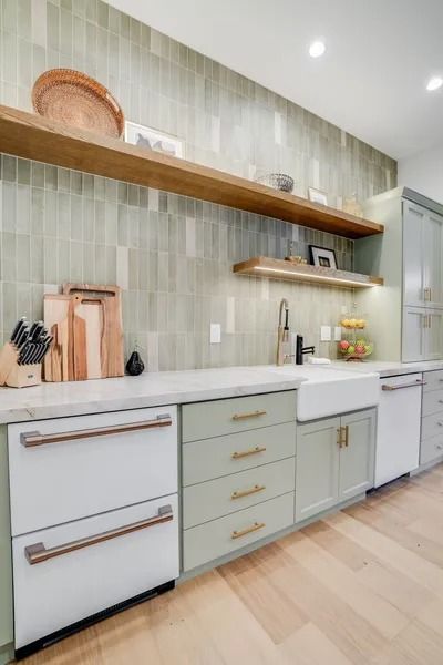 Kitchen with white countertops, green cabinets, wood shelves, and light green vertical tile backsplash.