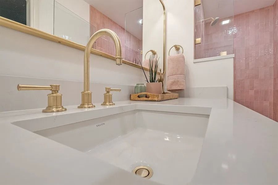 White bathroom sink with gold fixtures, pink tile wall, and mirror.
