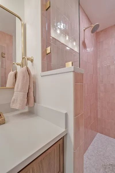Pink tiled bathroom with white countertop, gold fixtures, and shower.