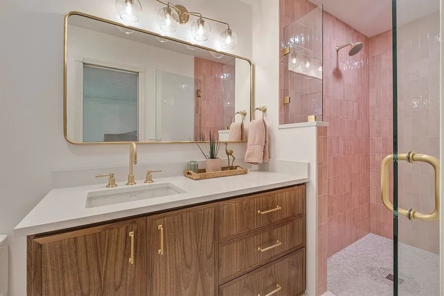 Bathroom with pink tile shower, gold fixtures, wood vanity, and a large mirror.