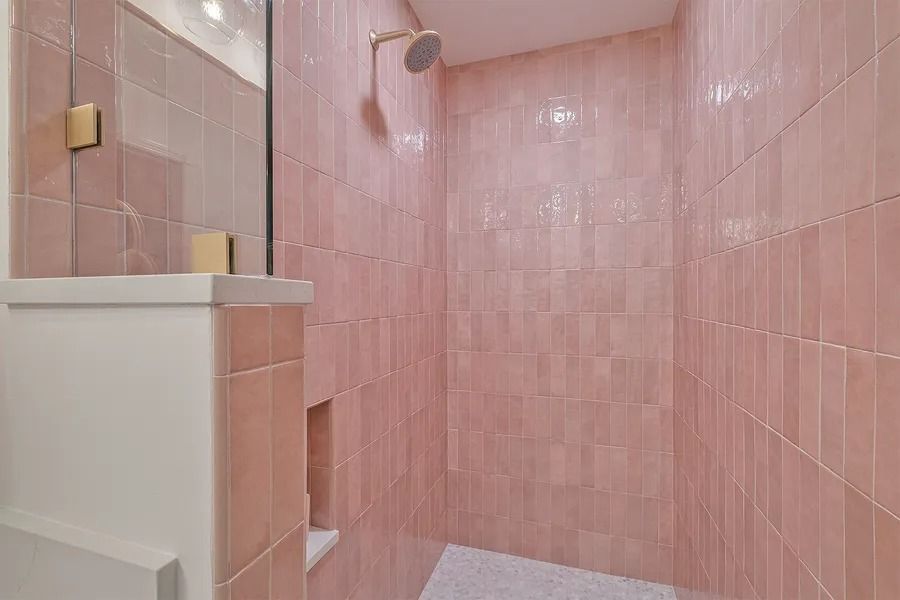 Pink tiled shower with a white shelf and gold showerhead.