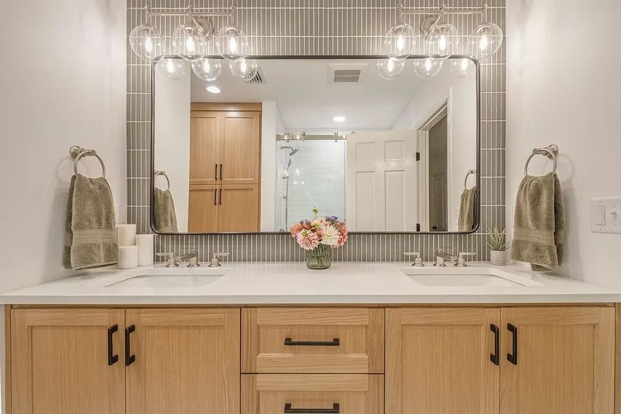 Bathroom with light wood vanity, white countertop, large mirror, and gray tile backsplash.