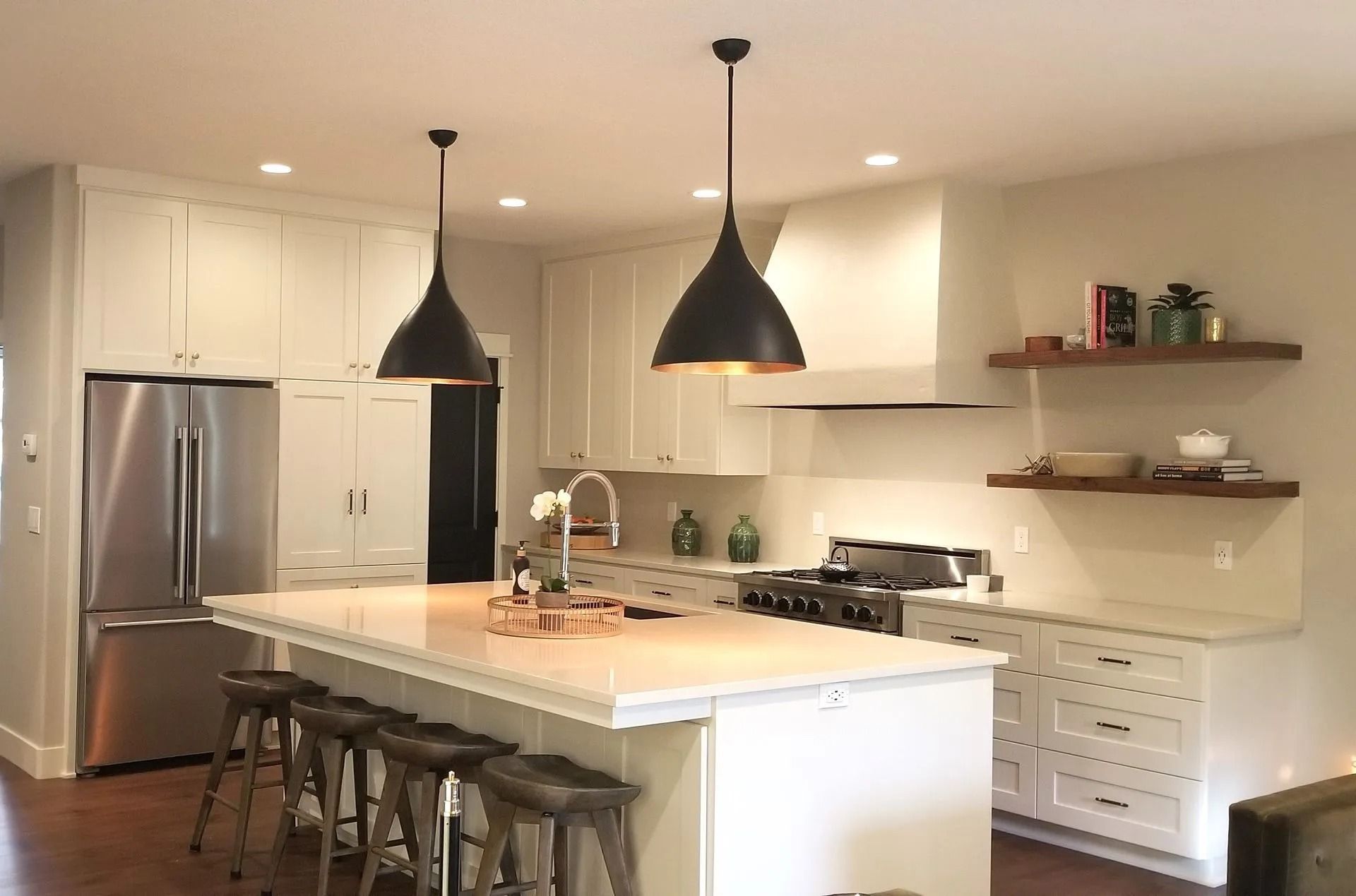 White kitchen with island, stainless steel appliances, dark pendant lights, and wooden shelves.