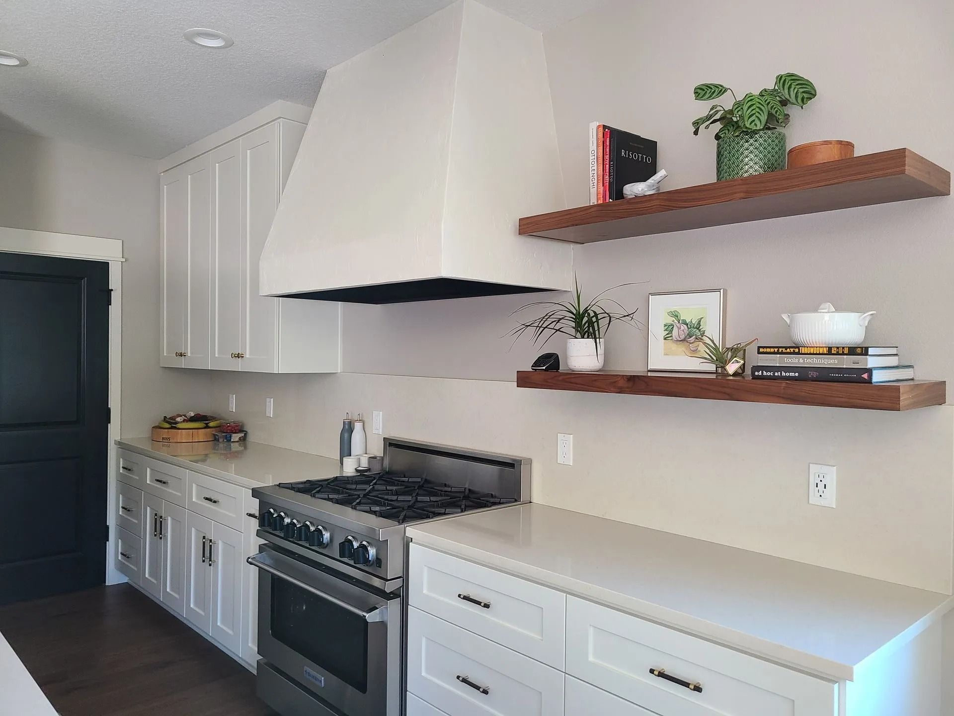 Kitchen with white cabinets, stainless steel range, and wood floating shelves with decor.