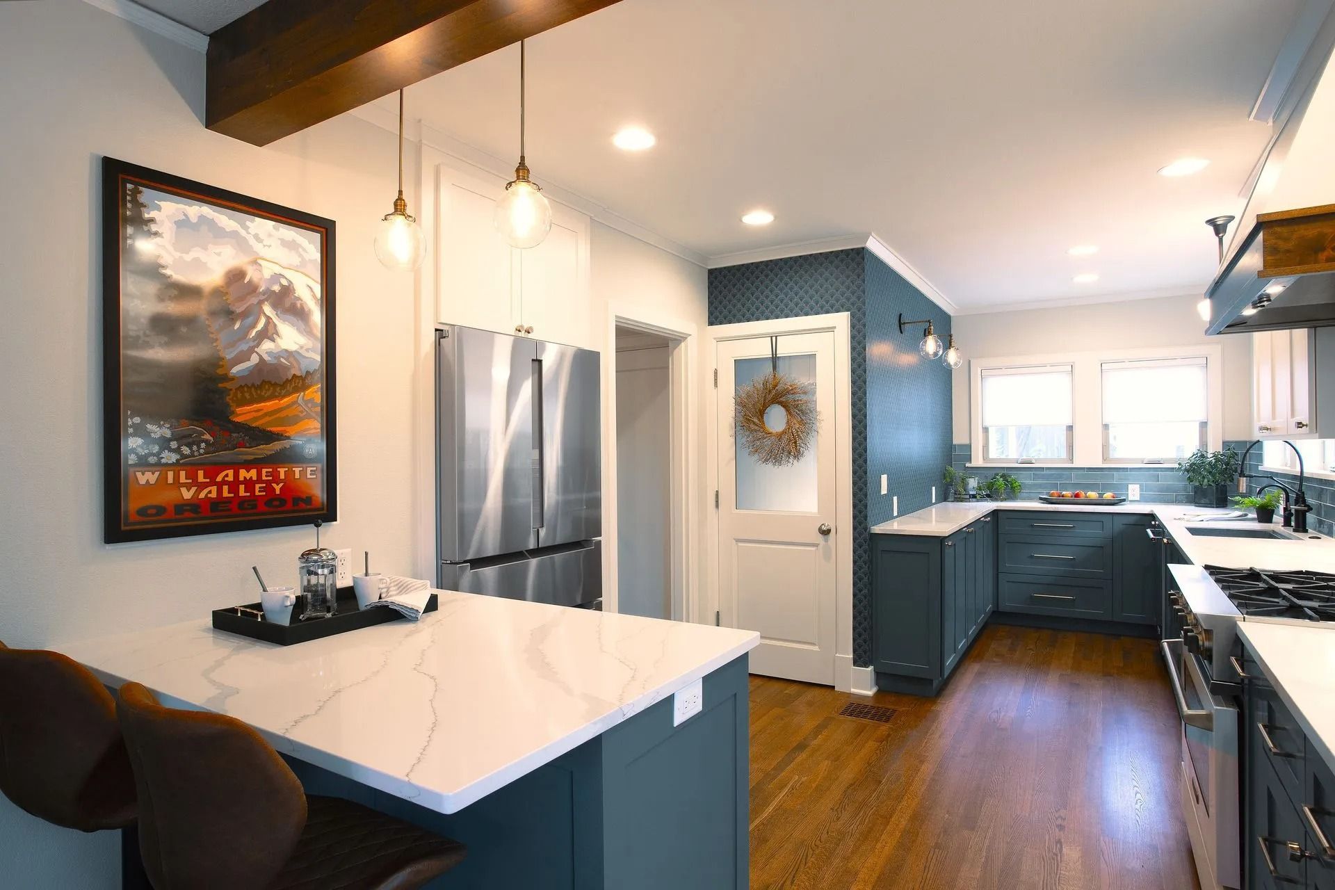 Modern kitchen with teal cabinets, white countertops, stainless steel appliances, and a poster.