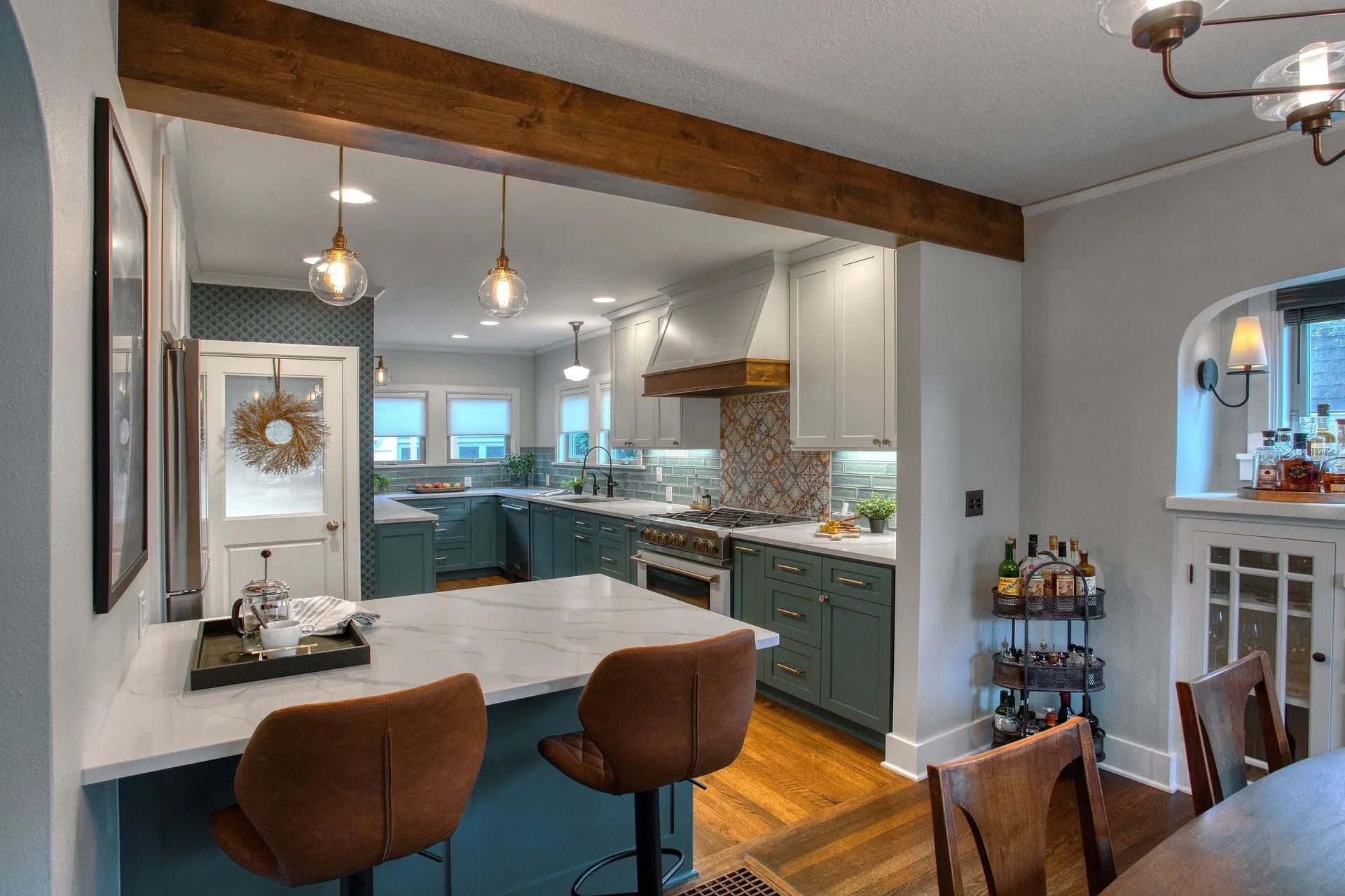 Kitchen renovation with teal cabinets, marble countertops, and brown leather bar stools.