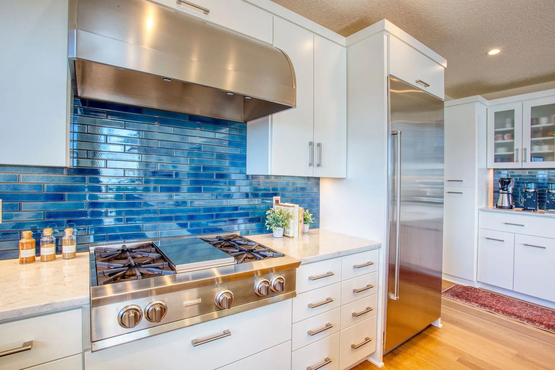 White kitchen with blue tiled backsplash, stainless steel appliances, and wood flooring.